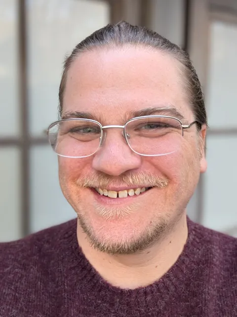 Will Yennie, smiling, in glasses and a maroon sweater
